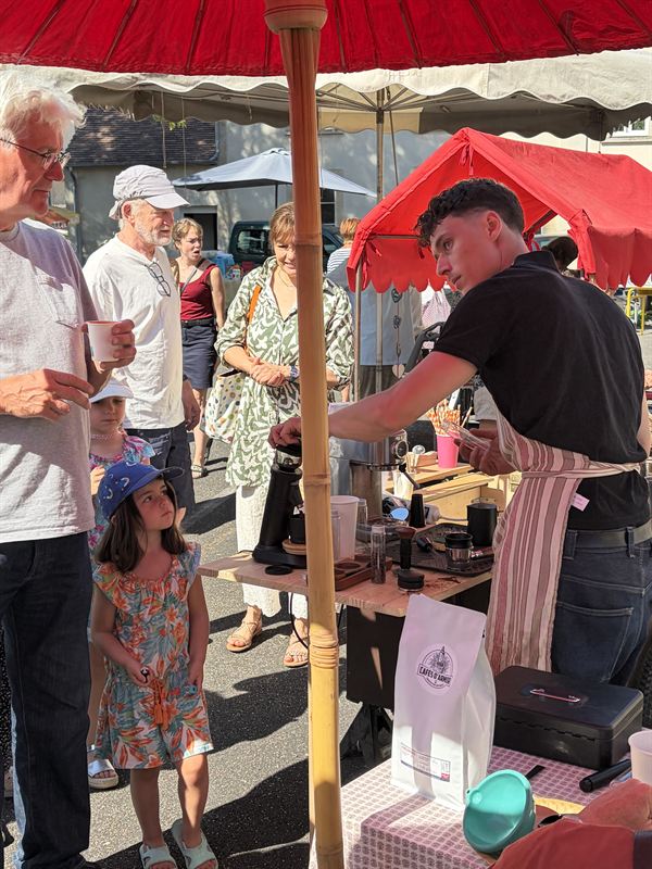 Service du café aux visiteurs d'un marché, sous le parasol rouge de Boé Coffee